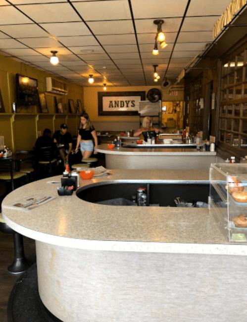Interior of a diner named "Andy's," featuring a curved counter, patrons seated, and a casual atmosphere.