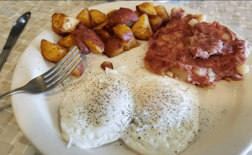 A plate with two poached eggs, hash browns, and seasoned roasted potatoes. Fork and knife on the side.