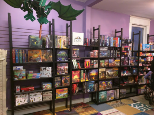 A colorful game store interior featuring shelves filled with various board games and a dragon decoration above.
