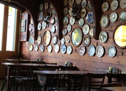 A cozy restaurant interior featuring wooden walls adorned with decorative plates and empty tables.