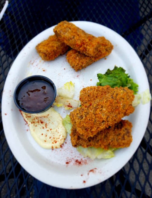 A plate of crispy fried food with dipping sauces, garnished with lettuce and sprinkled with seasoning.