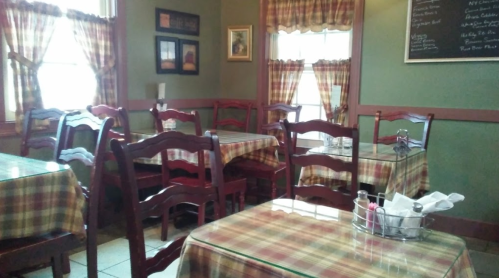 Cozy restaurant interior with wooden chairs and plaid tablecloths, featuring green walls and window curtains.