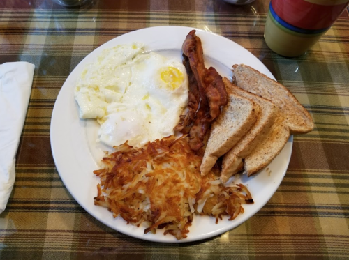 A plate of breakfast featuring eggs, bacon, toast, and hash browns on a checkered tablecloth.
