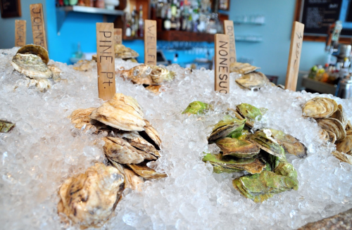 A display of fresh oysters on ice, labeled with wooden tags indicating their types and origins.