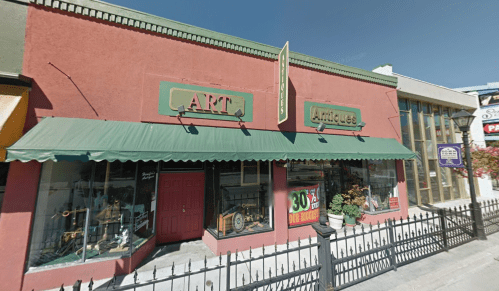 A storefront featuring "ART" and "Antiques" signs, with green awnings and large windows displaying various items.