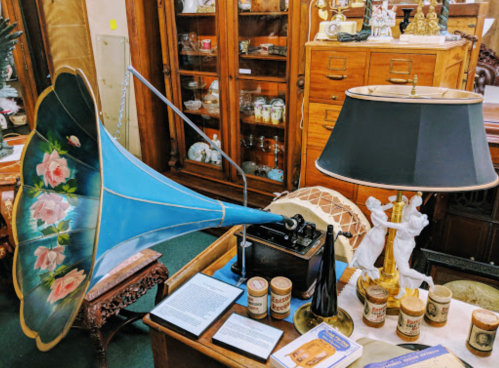 A vintage gramophone with a blue horn, a lamp, and various antique items displayed on a wooden table.