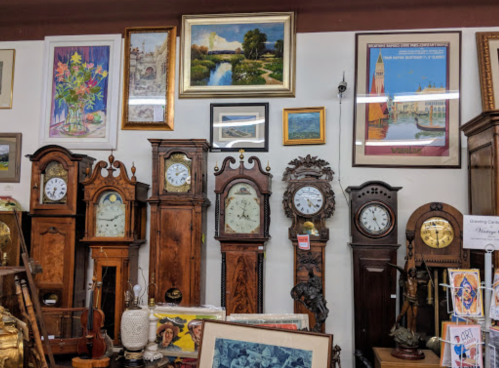 A collection of vintage clocks and framed artwork displayed on a wall in an antique shop.