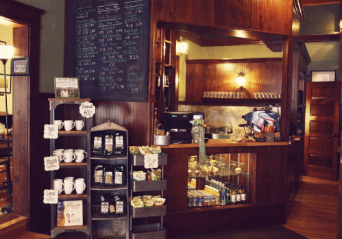 Cozy café interior with a wooden counter, menu board, and shelves displaying drinks and snacks. Warm, inviting atmosphere.