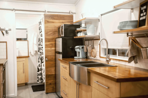 Modern kitchen with wooden countertops, stainless steel sink, black fridge, and open shelving displaying dishes.