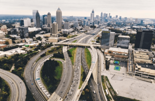 Aerial view of a busy highway interchange with Atlanta's skyline in the background on a cloudy day.