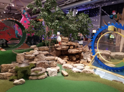 A colorful indoor play area featuring rocks, greenery, and playful structures for children.
