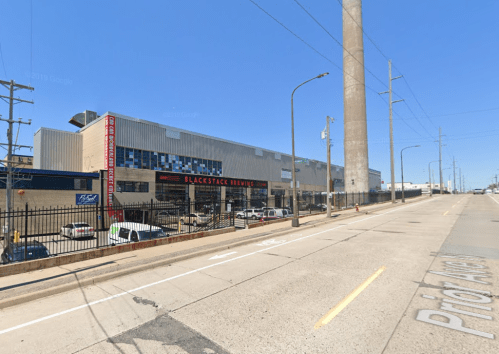 Exterior view of Blackstack Brewing, featuring a modern building and a clear blue sky, with cars parked nearby.