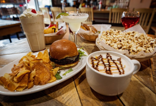 A table spread featuring a burger with chips, popcorn, a milkshake, a margarita, and a dessert in a bowl.