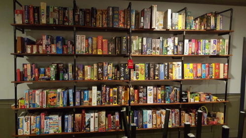 A large wooden shelf filled with various board games, neatly organized by title and color.