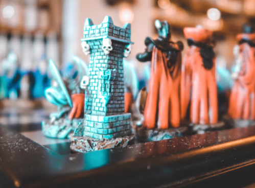 A close-up of a colorful miniature tower with skulls, surrounded by cloaked figures on a tabletop.