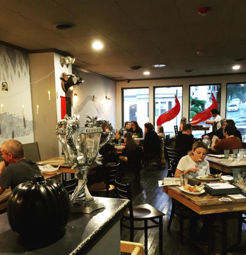 A cozy restaurant interior with diners, wooden tables, and a trophy on display, featuring red flags and candlelight.