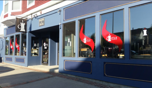 Exterior of a building with large windows featuring red flame decals and a sign reading "Castle." Bright, sunny day.