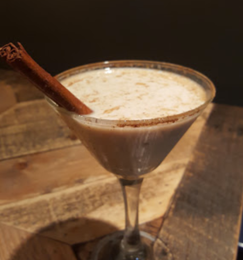 A creamy cocktail in a martini glass, garnished with a cinnamon stick and a sprinkle of cinnamon on the rim.