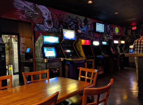 A dimly lit arcade with colorful vintage game machines and a wooden table in the foreground.