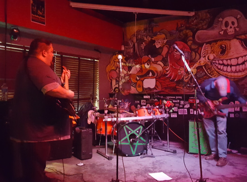 A band performs on stage in a vibrant venue with colorful murals and instruments, creating an energetic atmosphere.