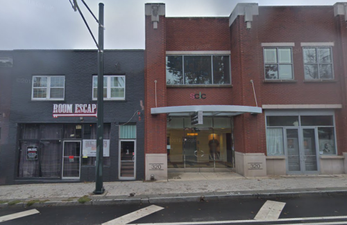A street view of two buildings: one with "Room Escape" signage and the other with a modern entrance labeled "320."