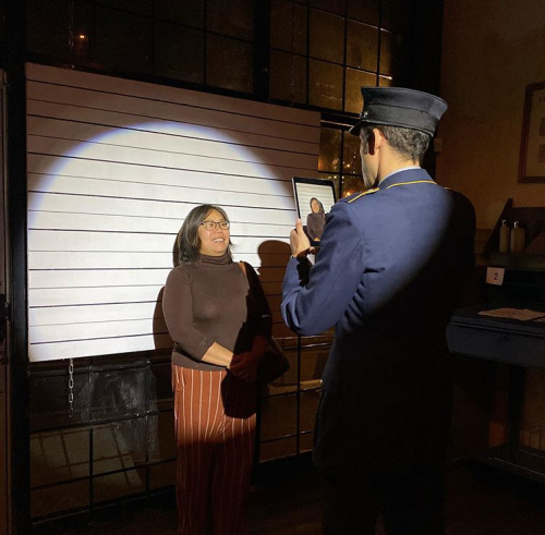 A woman poses for a photo in front of a spotlight, while a man in a uniform holds a framed picture.