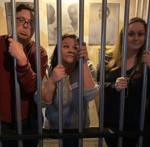 Three people playfully posing behind bars, with one making a silly face and the others looking amused.