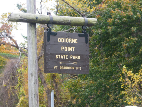 Wooden sign for Odiorne Point State Park, featuring directional arrows and surrounded by autumn foliage.