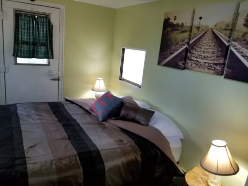 Cozy bedroom with a bed, decorative pillows, lamps, and artwork of a railway on the wall. Green walls and a window.