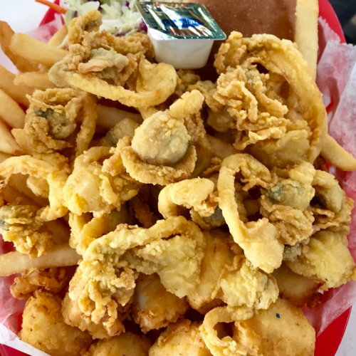A red plate filled with fried seafood, including calamari, fries, coleslaw, a roll, and a dipping sauce.