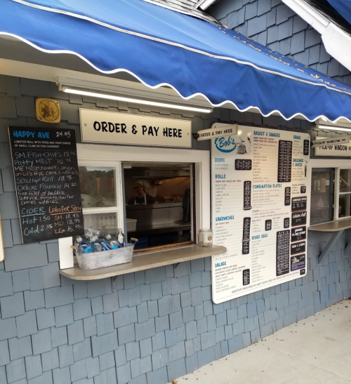 A food stand with a blue awning, menu board, and order window, featuring seafood options and drinks.