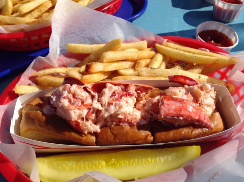 A basket of lobster rolls with fries and a pickle on a blue table.