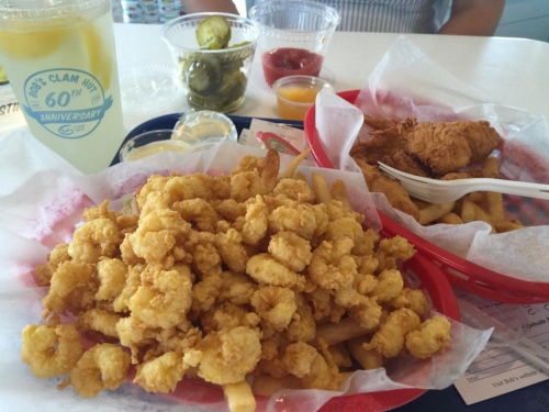 A plate of golden fried shrimp and fries, accompanied by pickles, dipping sauces, and a drink.