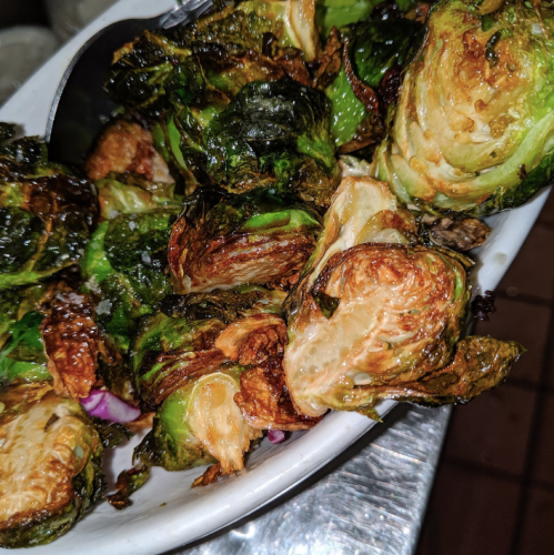 A close-up of roasted Brussels sprouts in a serving dish, showcasing their crispy, golden-brown leaves.
