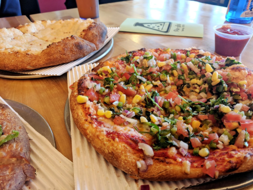 A close-up of two pizzas on a table: one topped with fresh vegetables and the other with a cheesy crust.