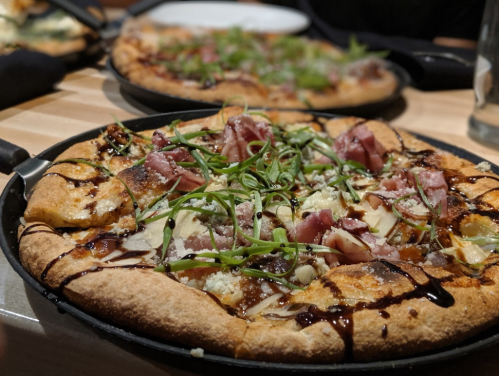 A close-up of a gourmet pizza topped with ham, cheese, and green onions, drizzled with balsamic glaze.
