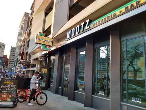 Exterior of Mootz Pizzeria & Bar with a bicycle delivery parked outside and a sign for Side Hustle Carry Out.
