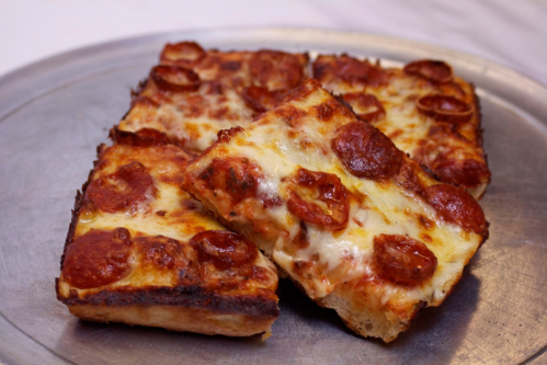 A silver platter with several slices of pepperoni pizza, featuring melted cheese and a crispy crust.