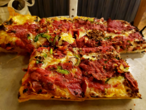 A close-up of a freshly baked pizza topped with cheese, pepperoni, vegetables, and herbs, with a knife resting on it.