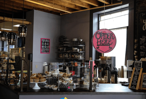 Cozy café interior with a display of pastries, a sign reading "Open Here," and a welcoming atmosphere.