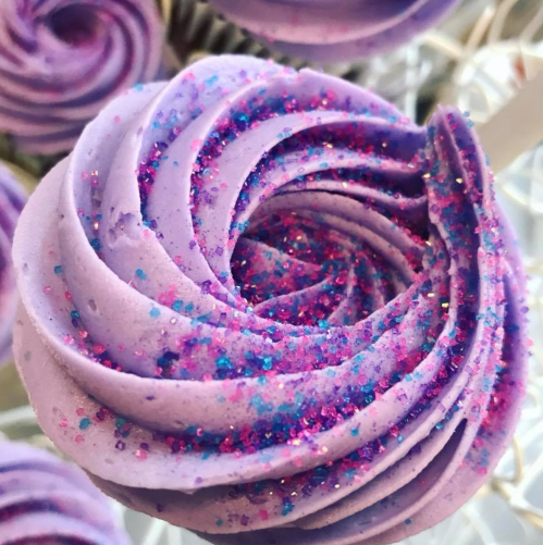 A close-up of a purple swirl cupcake topped with colorful glitter sprinkles.