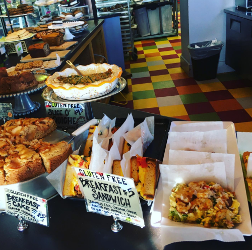 A colorful display of gluten-free baked goods, including cakes, quiches, and breakfast sandwiches on a café counter.