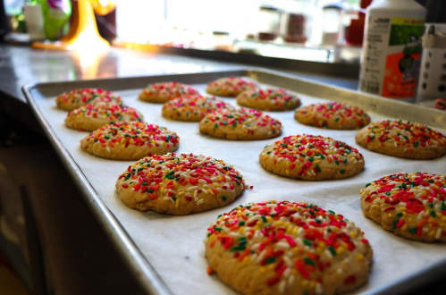 A tray of freshly baked cookies topped with colorful sprinkles, resting on parchment paper in a bright kitchen.