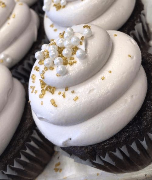 Close-up of chocolate cupcakes topped with light pink frosting, decorated with edible pearls and gold sprinkles.