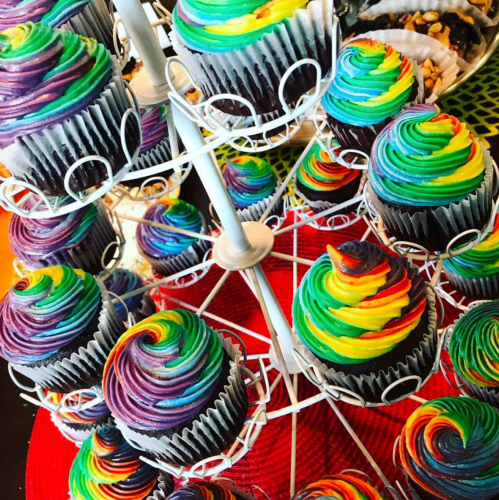 A colorful display of cupcakes with vibrant rainbow swirls on top, arranged on a white stand.