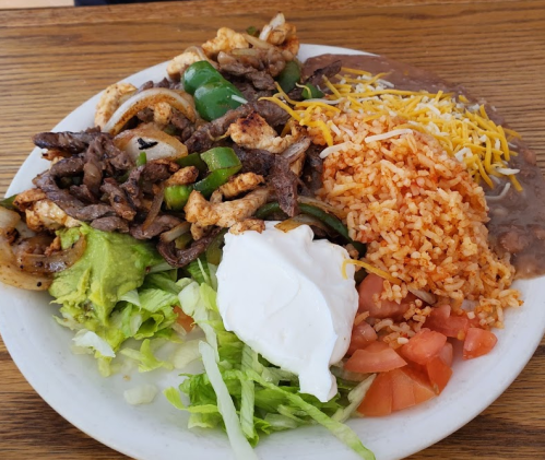 A plate of Mexican food featuring grilled meat, rice, beans, lettuce, tomatoes, guacamole, and sour cream.