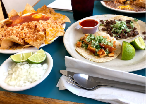 A plate of tacos with onions and lime, served with rice and tortilla chips on a blue table.