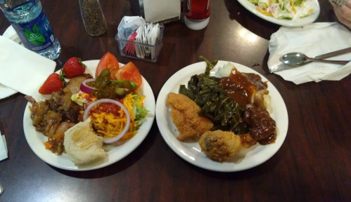 A plate of fried chicken, collard greens, and a side of gravy, alongside a salad with strawberries and vegetables.
