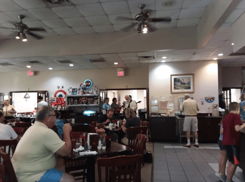 A busy restaurant interior with patrons dining, a buffet area, and people chatting near the counter.