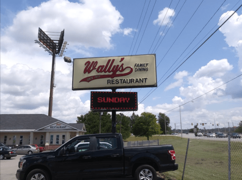 Sign for Wally's Family Dining Restaurant with a digital display showing "SUNDAY" and a pickup truck parked nearby.